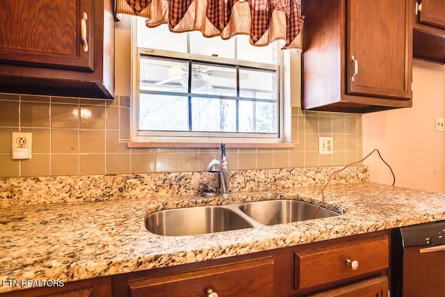 kitchen featuring black dishwasher, light stone counters, backsplash, and a sink