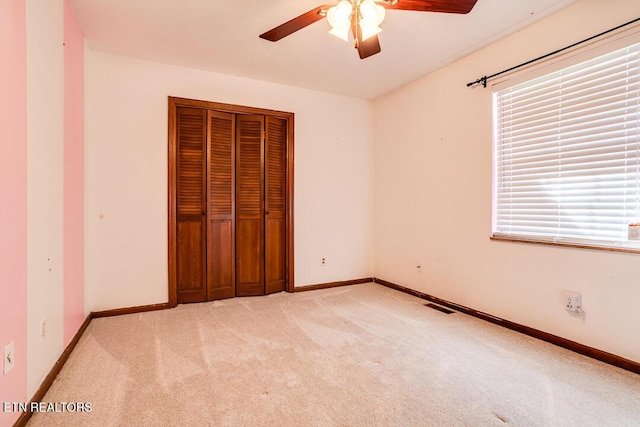 unfurnished bedroom with a closet, visible vents, light carpet, ceiling fan, and baseboards