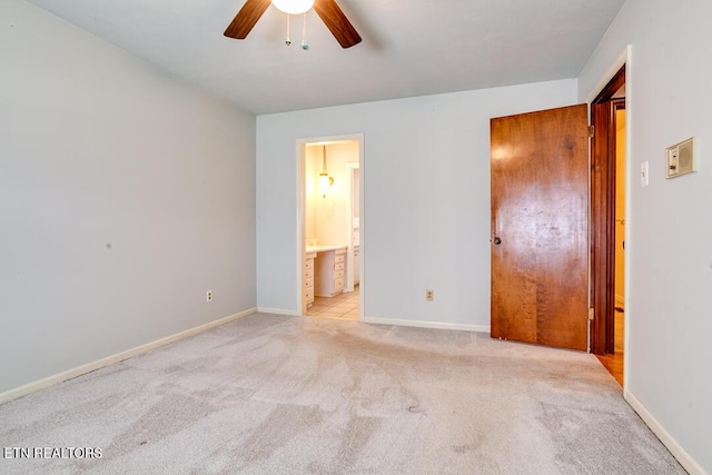 unfurnished bedroom with light carpet, ensuite bath, baseboards, and a ceiling fan