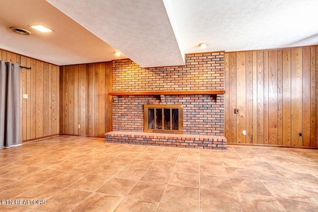 unfurnished living room featuring a fireplace, wooden walls, a textured ceiling, baseboards, and tile patterned floors