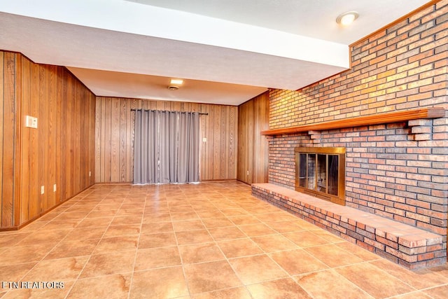 unfurnished living room featuring wood walls, brick wall, a brick fireplace, and tile patterned floors