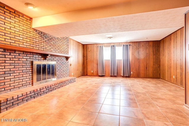 unfurnished living room featuring a brick fireplace, light tile patterned flooring, wooden walls, and brick wall