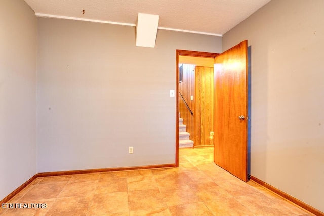 spare room with stairs, baseboards, and a textured ceiling