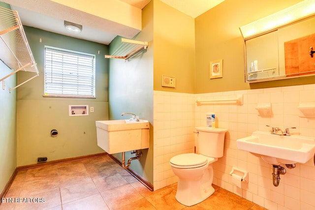 bathroom with toilet, a wainscoted wall, a sink, tile patterned flooring, and tile walls