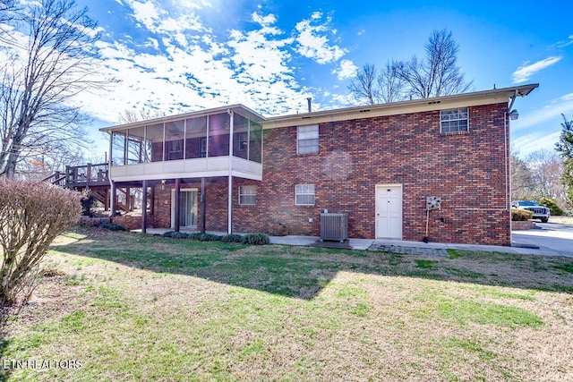 rear view of house featuring brick siding, a lawn, central AC unit, a sunroom, and a patio area