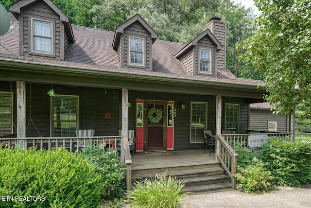 cape cod home with a porch, roof with shingles, and a chimney