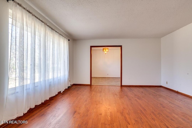 empty room with a textured ceiling, baseboards, and wood finished floors