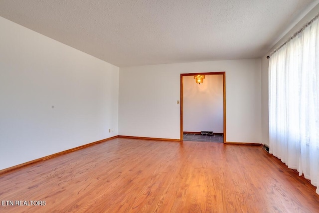 spare room with light wood finished floors, baseboards, and a textured ceiling