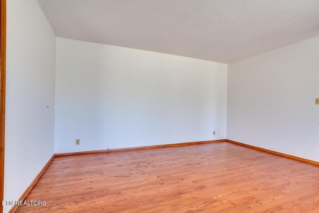 empty room with light wood-style floors, baseboards, and a textured ceiling