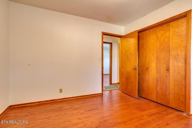 unfurnished bedroom with light wood finished floors, a textured ceiling, baseboards, and a closet