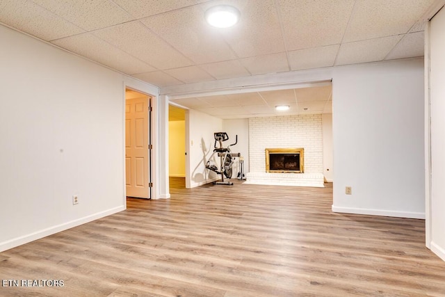 finished below grade area featuring a paneled ceiling, a brick fireplace, baseboards, and wood finished floors