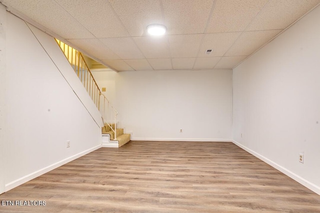 finished below grade area featuring a paneled ceiling, baseboards, stairway, and wood finished floors