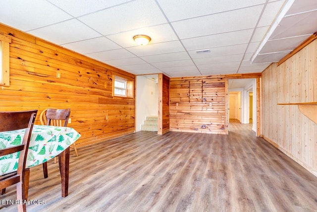 interior space featuring a drop ceiling, wood walls, wood finished floors, visible vents, and stairway