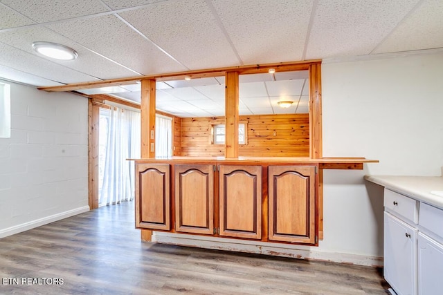 kitchen featuring concrete block wall, baseboards, brown cabinets, wood finished floors, and light countertops