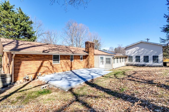 rear view of house featuring a patio area, brick siding, and a chimney