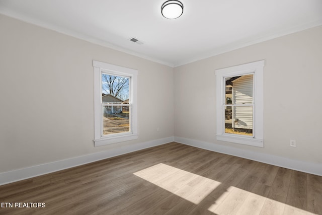 spare room with crown molding, wood finished floors, visible vents, and baseboards