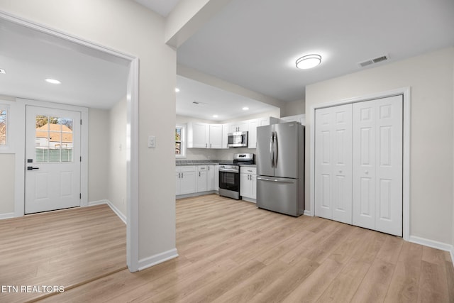 kitchen with stainless steel appliances, light wood-type flooring, white cabinetry, and visible vents