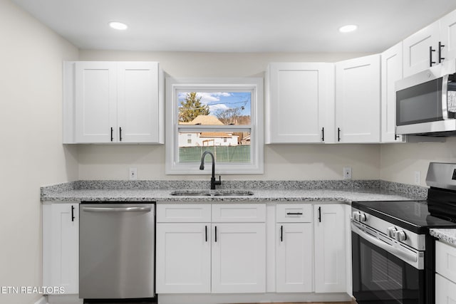 kitchen with light stone counters, recessed lighting, stainless steel appliances, a sink, and white cabinets