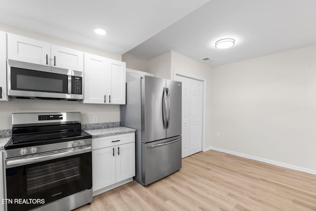 kitchen featuring appliances with stainless steel finishes, light wood-style flooring, white cabinetry, and light stone countertops