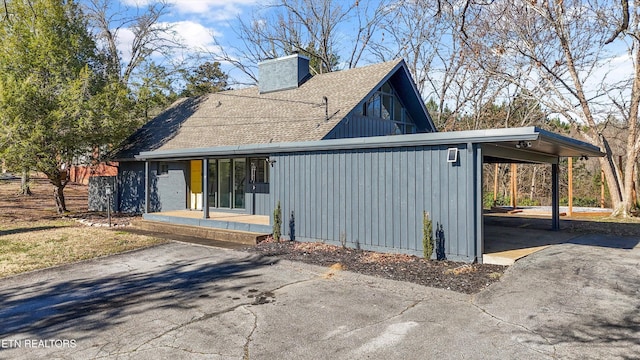 view of side of property with driveway, a chimney, roof with shingles, a carport, and board and batten siding