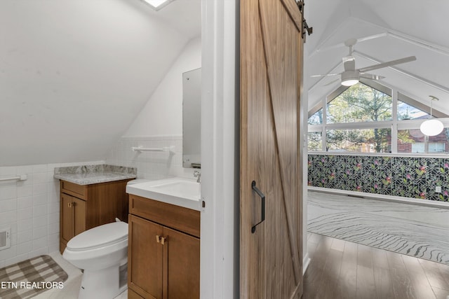 half bathroom featuring a ceiling fan, toilet, vaulted ceiling, vanity, and tile walls