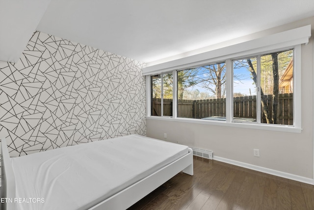 bedroom with visible vents, an accent wall, dark wood-type flooring, baseboards, and wallpapered walls