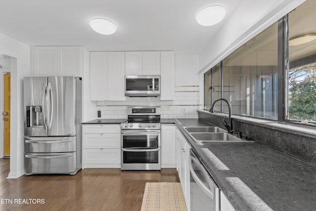 kitchen featuring stainless steel appliances, dark countertops, dark wood-type flooring, white cabinetry, and a sink