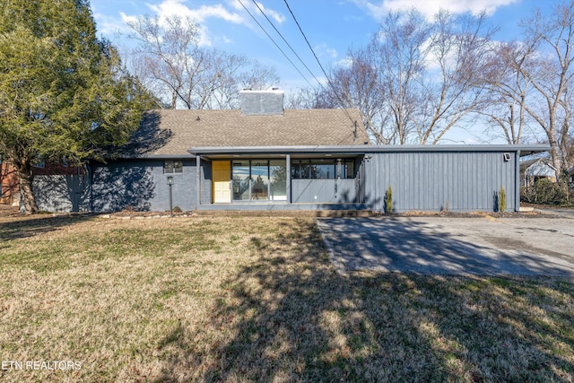 back of property featuring a shingled roof, a lawn, and a chimney