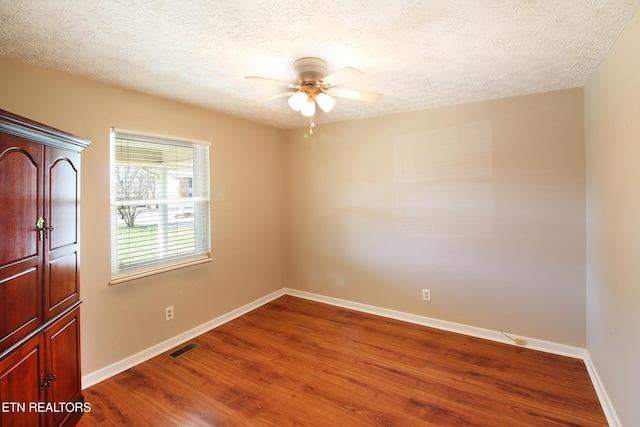 spare room with a textured ceiling, dark wood finished floors, and baseboards