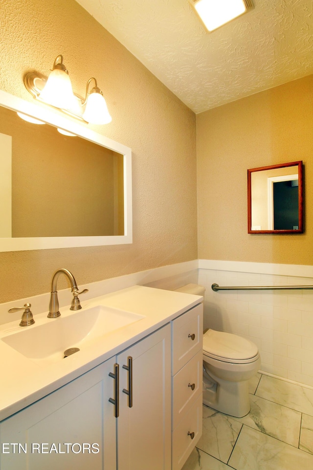 bathroom with wainscoting, toilet, marble finish floor, a textured ceiling, and vanity