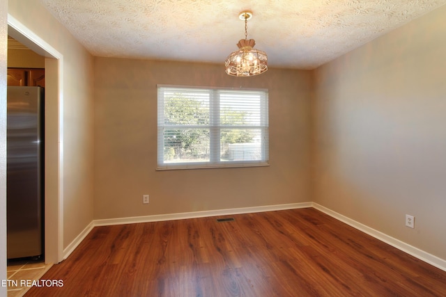 empty room featuring a textured ceiling, baseboards, and wood finished floors