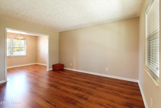 unfurnished room with a textured ceiling, dark wood-style flooring, and baseboards