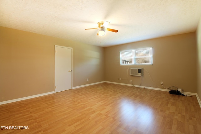 unfurnished room with a textured ceiling, a wall unit AC, baseboards, and light wood-style floors