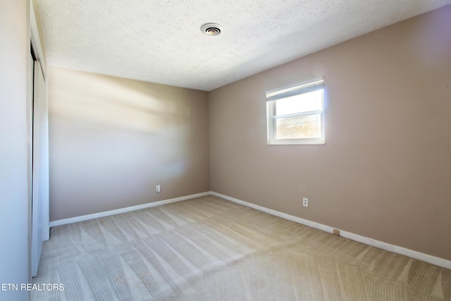 carpeted empty room featuring a textured ceiling, visible vents, and baseboards