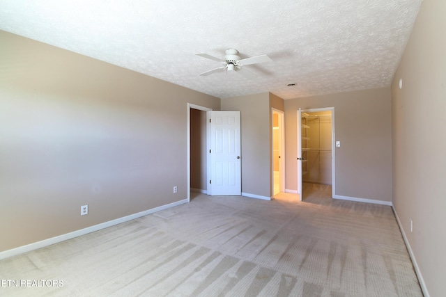 unfurnished bedroom featuring a textured ceiling, light carpet, baseboards, a spacious closet, and a closet