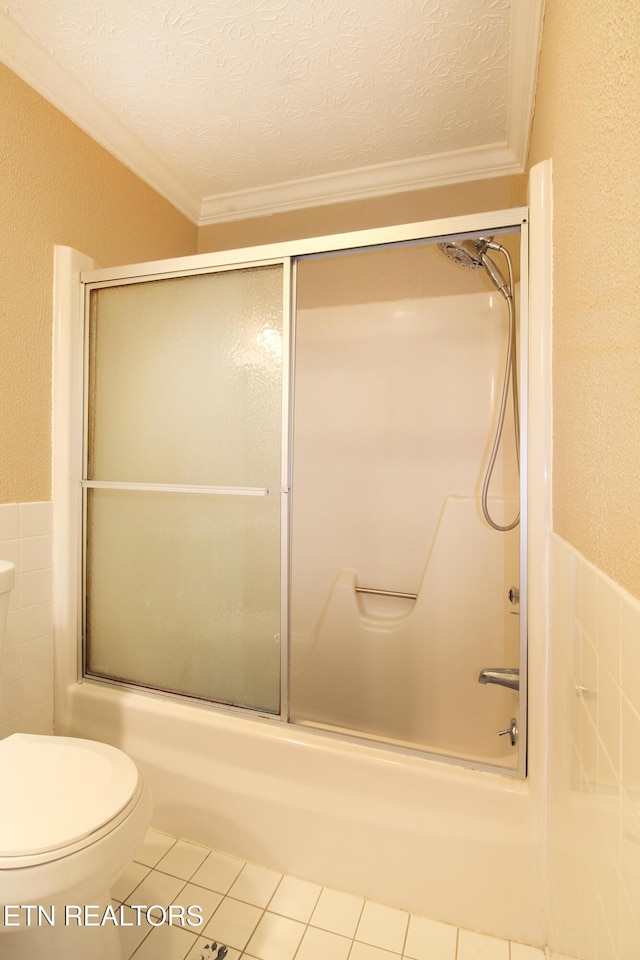 bathroom featuring bath / shower combo with glass door, toilet, tile patterned floors, a textured ceiling, and tile walls