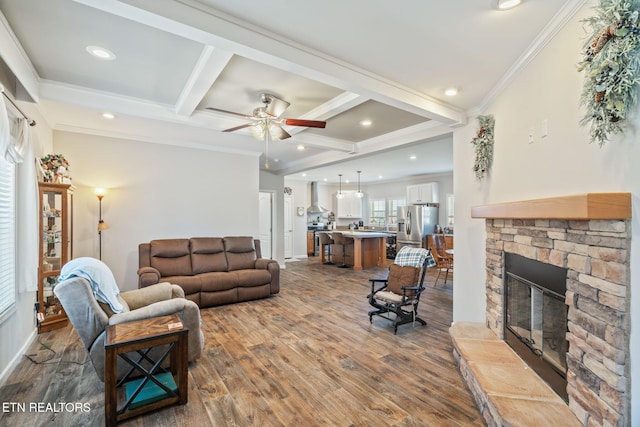 living room with a stone fireplace, coffered ceiling, wood finished floors, beam ceiling, and crown molding