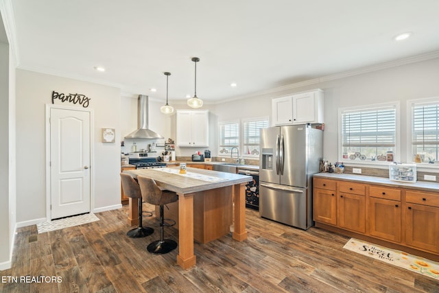 kitchen featuring dark wood-style floors, crown molding, wall chimney exhaust hood, stainless steel appliances, and a kitchen bar