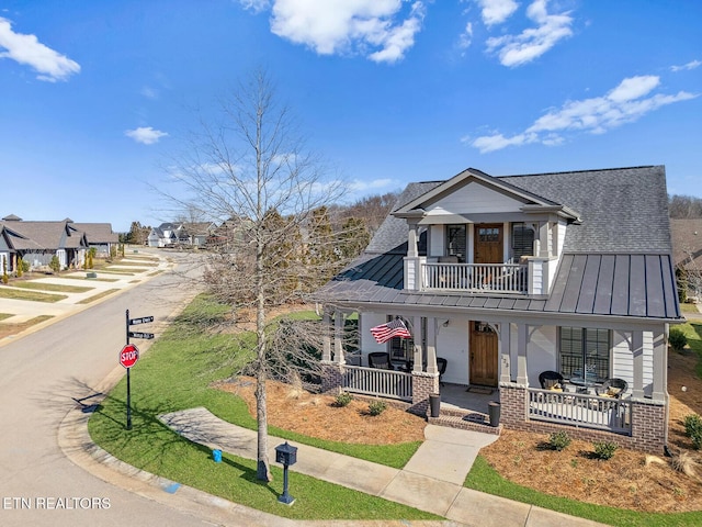 view of front facade with metal roof, a balcony, covered porch, brick siding, and a standing seam roof