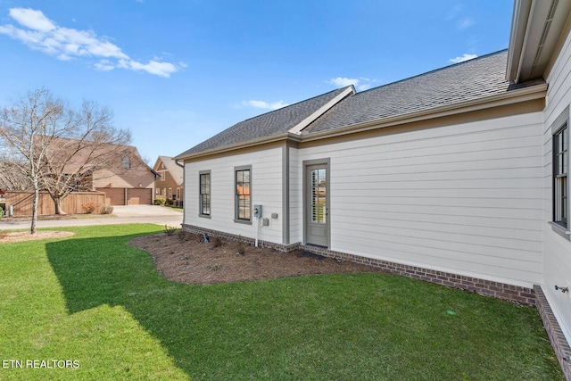 rear view of property featuring a shingled roof, fence, and a yard