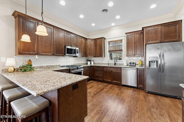 kitchen with decorative light fixtures, stainless steel appliances, visible vents, a sink, and a peninsula