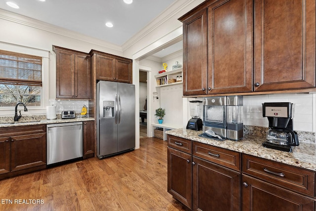 kitchen with light wood-type flooring, crown molding, stainless steel appliances, and a sink