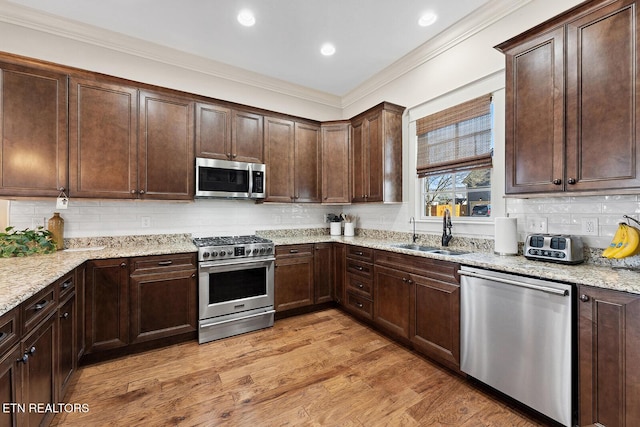 kitchen with light wood finished floors, tasteful backsplash, appliances with stainless steel finishes, ornamental molding, and a sink