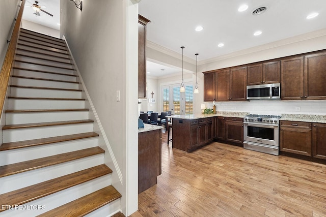 kitchen with light stone counters, tasteful backsplash, hanging light fixtures, appliances with stainless steel finishes, and light wood-type flooring