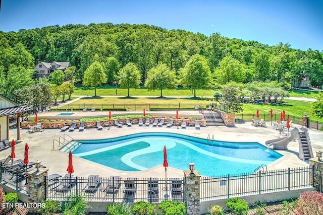 pool featuring a yard, a hot tub, a patio area, fence, and a water slide