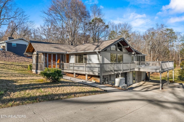 view of front of house featuring a sunroom, a shingled roof, a deck, and concrete driveway