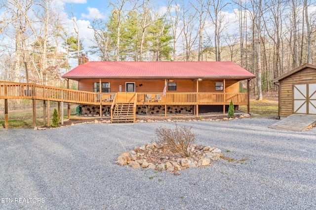 chalet / cabin featuring an outbuilding, gravel driveway, covered porch, a chimney, and metal roof