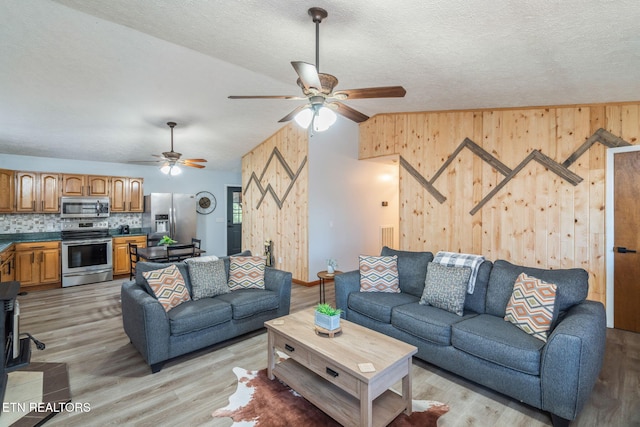 living area with wooden walls, a textured ceiling, a ceiling fan, and light wood-style floors