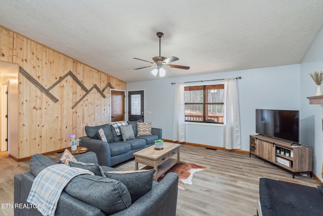 living room featuring wood walls, a textured ceiling, baseboards, and wood finished floors