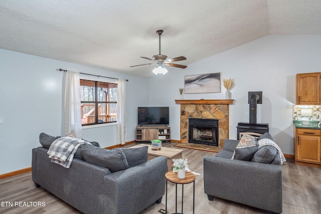 living room featuring a ceiling fan, wood finished floors, baseboards, vaulted ceiling, and a textured ceiling